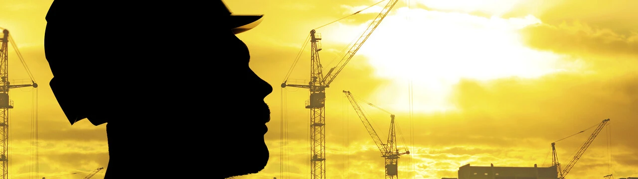 Silueta de un obrero con grúas de construcción detrás