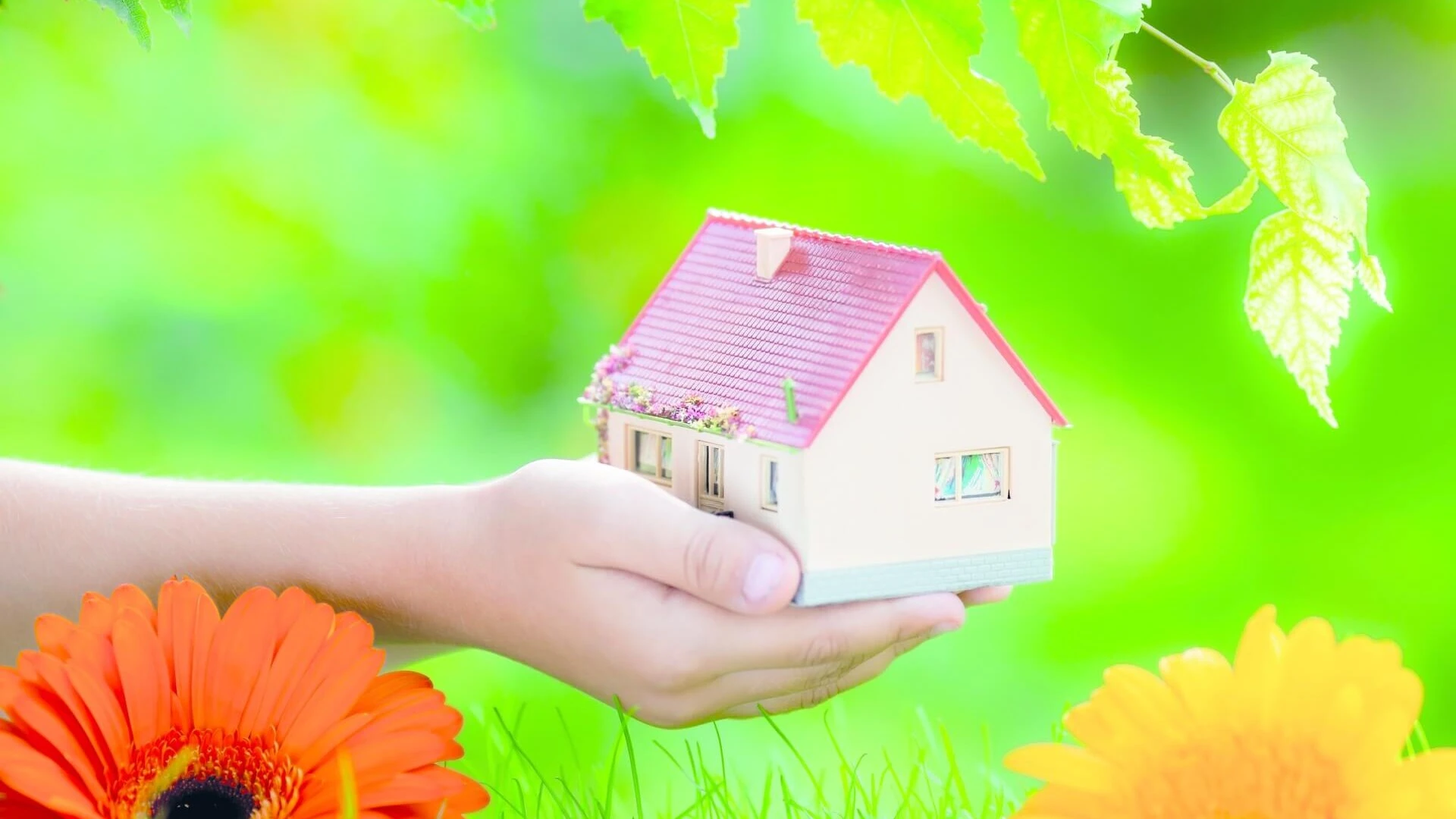 Mano sujetando una casa rodeada de flores