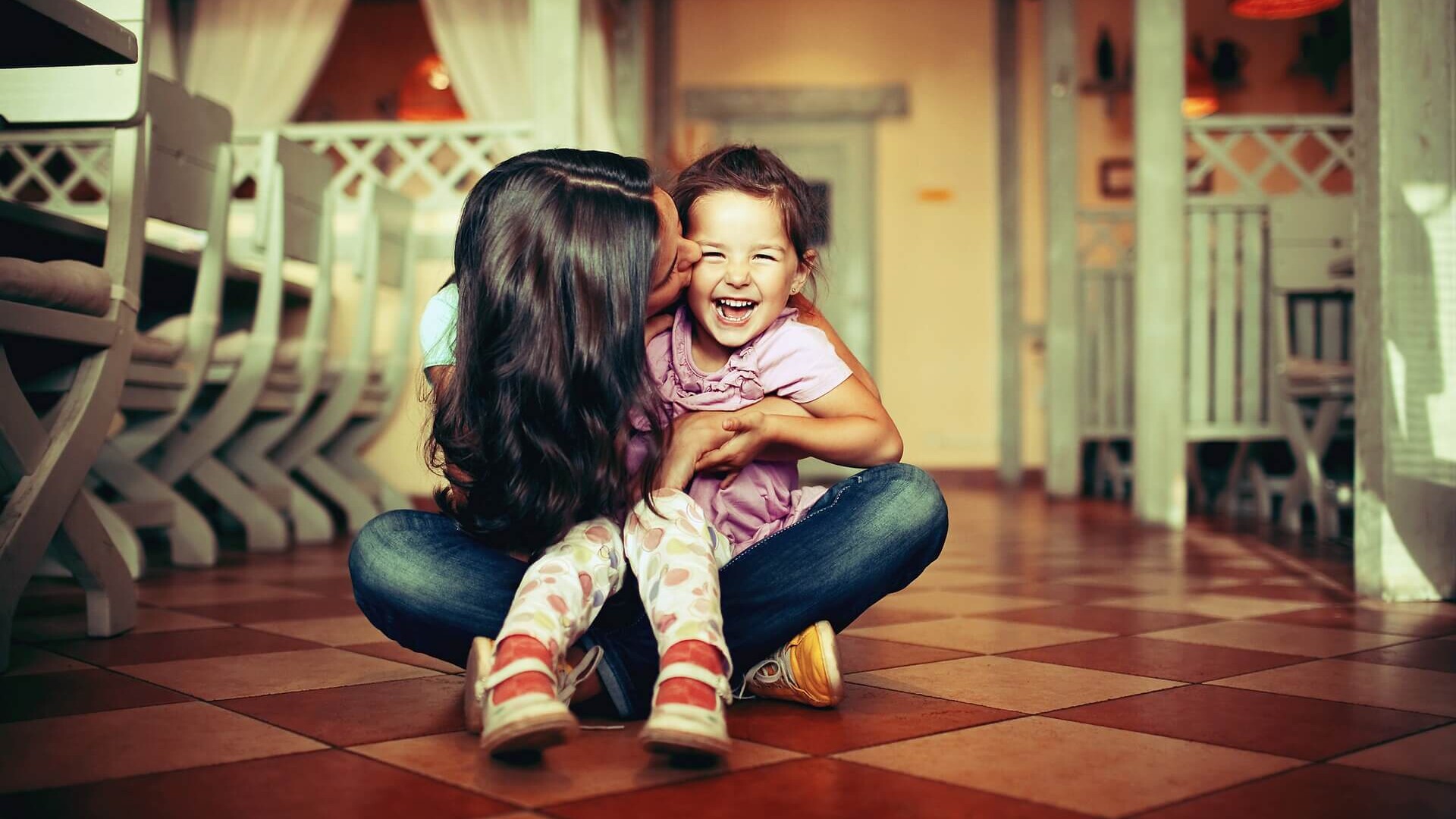 Mujer besando a una niña sentadas en el suelo Mujer besando a una niña sentadas en el suelo