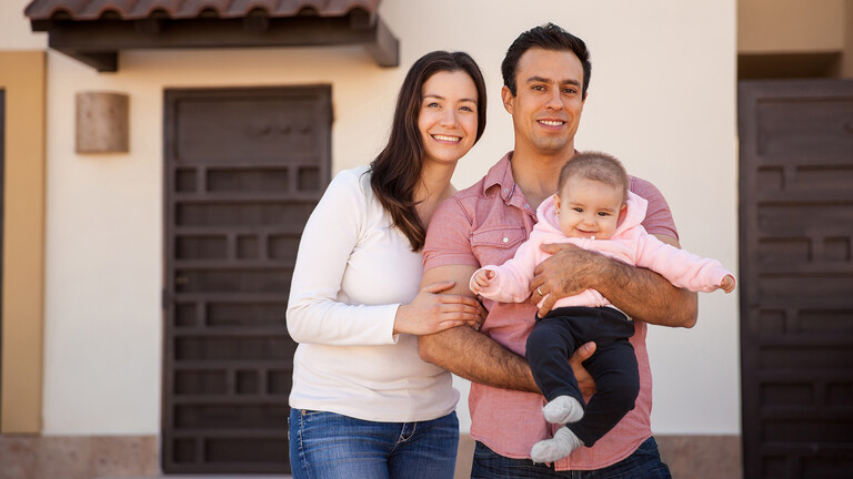 Familia posando delante de casa con su bebé en brazos Familia posando delante de casa con su bebé en brazos